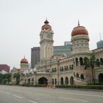 a large building with a clock tower with Merdeka Square, Kuala Lumpur in the background